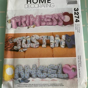 May include: A McCall's Home Decorating pattern envelope featuring the word "PRINCESS" in pink fabric letters, "JUSTIN" in newspaper print letters, and "ANGEL" in blue floral fabric letters. The number 3274 is visible.