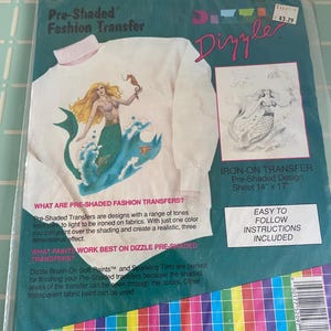 May include: A pre-shaded iron-on fashion transfer featuring a mermaid design. The transfer sheet is 14 inches by 17 inches. The package includes instructions for use.  The text on the package reads "Pre-Shaded Fashion Transfer" and "Dizzle".