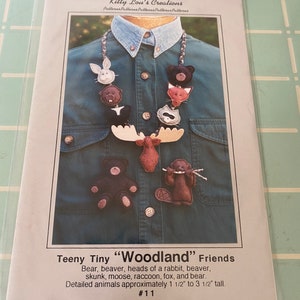 May include: A pattern for a set of felt woodland animal ornaments. The pattern includes instructions for making a bear, beaver, rabbit, skunk, moose, raccoon, fox, and bear. The animals are approximately 1 1/2 inches to 3 1/2 inches tall. The pattern is titled "Teeny Tiny "Woodland" Friends" and is numbered #11.