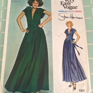 May include: Vintage Vogue sewing pattern featuring a Stan Herman design. The pattern cover displays a woman in a green, floor-length dress with a deep V-neck and a matching belt. The text "Very Easy Vogue" and "American Designer Original" are also visible.
