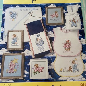 May include: A collection of cross-stitch patterns featuring angels and baby-themed designs. The patterns include "Bless the Baby", "Welcome Little One", "Our Little Cupcake", and "Kaitlin Anne Jones, She's So..."