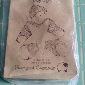 May include: A brown paper package features a bear in pajamas illustration holding a star. Text reads "Sleep Tight" and "5" Bear in PJ's with a 2" wood star." The package also has a sheep logo and "Farmyard Creations" text.