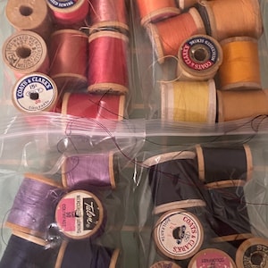 May include: A close-up of two bags of assorted spools of thread. The spools are in various colors, including black, white, pink, red, yellow, and blue. The spools are labeled with the brand names "Coats & Clarks", "Talon", and "Bellfast".