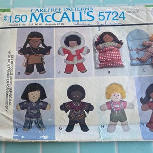 May include: A vintage McCall's sewing pattern for making a set of dolls and a sleeping bag. The pattern number is 5724 and the price is $1.50. The pattern includes instructions for making six different dolls, including a Native American doll, a Santa doll, a girl doll in a red and white gingham dress, a boy doll in pajamas, a girl doll in a blue and white dress, and a boy doll in overalls. The pattern also includes instructions for making a sleeping bag for the dolls.