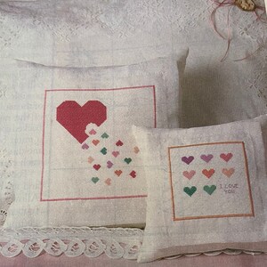 May include: Two white pillow covers with embroidered hearts. One pillow has a large red heart with smaller hearts falling from it. The other pillow has a row of colorful hearts and the text "I love you".