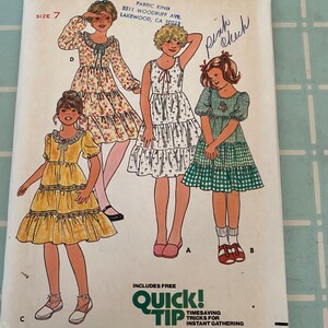 May include: A vintage sewing pattern for girls' dresses. The pattern is for size 7 and includes three different styles: a yellow dress with a ruffled skirt, a white dress with a tiered skirt, and a green and white gingham dress with a ruffled skirt. The pattern is from Butterick and is number 6090.