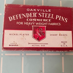 May include: A red box with white lettering that reads "Oakville Defender Steel Pins Commerce for Heavy Weight Fabrics". The box also says "Nickel Plated", "Sharp Points", "A product of Scovill", "Actual Size", and "Made in U.S.A.".