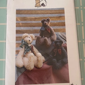 May include: A sewing pattern for three antique bears. The pattern is titled "A Stitch In Time" and is numbered #144. The bears are brown, white, and black. The pattern is on a striped background.