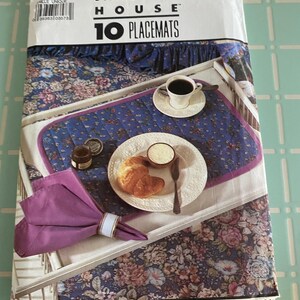 May include: A Simplicity House package for 10 placemats. The placemats feature a floral design on a blue backdrop. A tray with coffee, a plate with a croissant, butter, and a napkin with a ring are displayed on the placemats.