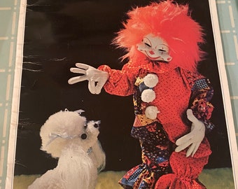 May include: A vintage book cover featuring a red and white clown doll with pink hair and a white poodle doll. The book title is "Loveable Stuffables" with the text "Pampered Poodle, Page 9" and "Clancy, Page 25" at the bottom.