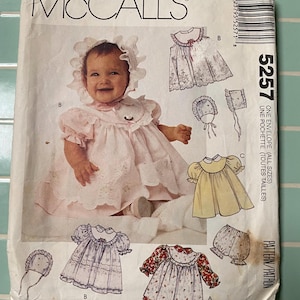 May include: A vintage McCall's sewing pattern envelope featuring a baby in a pink dress and bonnet. The pattern includes illustrations of baby dresses, bonnets, and bloomers. The envelope is labeled with the number 5257.