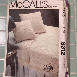 May include: A vintage McCall's sewing pattern envelope featuring a bedspread and pillow design. The envelope displays a cream-colored bedspread and pillows with embroidered floral patterns. The text "McCall's" is prominently displayed at the top.
