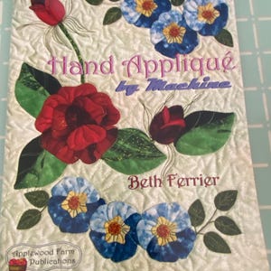 May include: A book cover titled "Hand Applique by Machine" featuring floral designs in red, blue, and yellow. The cover includes the author's name, Beth Ferrier, and the publisher's logo, Applewood Farm Publications.