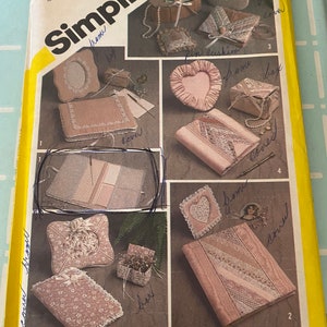 May include: A Simplicity sewing pattern for making various fabric boxes and covers. The pattern includes instructions for making a heart-shaped box, a square box, a rectangular box, and a book cover. The pattern is illustrated with photos of the finished projects.