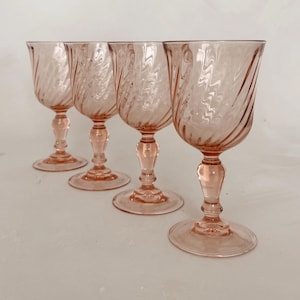 May include: Four pink-tinted stemmed glasses with a spiral design on the bowl. The glasses have a rounded base and a detailed stem. The glassware is arranged in a row, showcasing a vintage aesthetic.