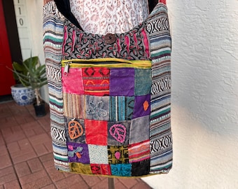 Puede incluir: Un bolso de hombro de tela de patchwork colorido con un bolsillo con cremallera y un borde a rayas blanco y negro. El bolso está hecho de diferentes telas con varios patrones y colores, incluyendo rojo, verde, azul, morado y amarillo.