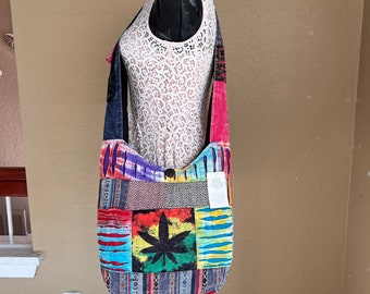 Puede incluir: Una bolsa de lona de patchwork multicolor con un gran diseño de hoja de marihuana verde. La bolsa está hecha de algodón y tiene una correa larga.