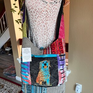 Può includere: Una borsa a tracolla in patchwork multicolore con una tasca con cerniera che presenta un'illustrazione di un cane blu e oro. La borsa ha una tracolla lunga ed è realizzata con diversi tessuti, tra cui denim, cotone e twill.