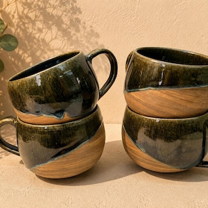 May include: Four ceramic mugs with a rounded shape and a handle on the side. Each mug features a two-tone design with a glossy, dark forest green glaze on the upper portion and a natural, unglazed tan clay finish on the lower portion.