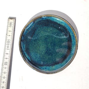 May include: Round ceramic dish with a teal and green glaze. The dish has a dark rim and a textured surface. A ruler is placed next to the dish, showing measurements in inches.