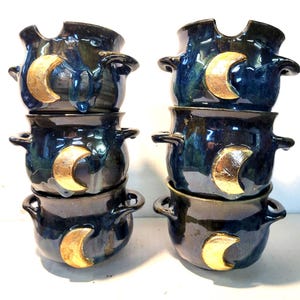 Könnte beinhalten: Sechs dunkelblaue Keramikschalen mit goldenen Halbmond-Akzenten, gestapelt in zwei Säulen. Jede Schale hat zwei Griffe und eine glänzende Oberfläche. Die Schalen sind ca. 15 cm im Durchmesser.