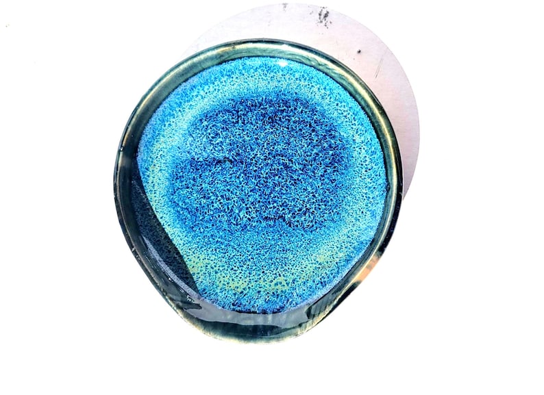 May include: A handmade, oval-shaped ceramic dish with a vibrant blue and turquoise interior. The dish has a textured surface and a dark, glossy rim. The design resembles an abstract underwater scene, perfect for serving small portions or as a decorative piece.
