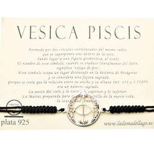 Może przedstawiać: Bransoletka ze sznurka w kolorze czarnym z zawieszką ze srebra przedstawiającą symbol Vesica Piscis. Zawieszka jest otoczona kółkiem z tekstem "Vesica Piscis" i opisem symbolu w języku hiszpańskim. Bransoletka jest oznaczona jako "plata 925" i "Hecho".