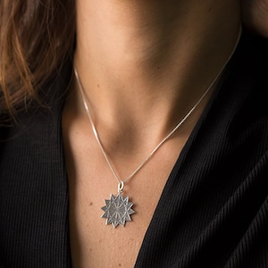 Op de afbeelding: Een zilveren ketting met een stervormige hanger. De hanger is versierd met ingewikkelde geometrische patronen.