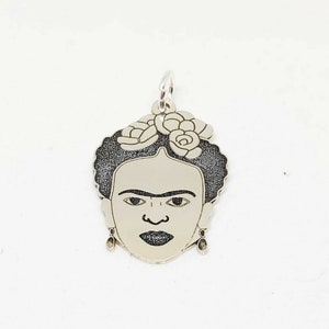 Puede incluir: Encanto de plata con un retrato en blanco y negro de Frida Kahlo con flores en el pelo.