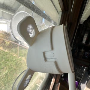 May include: White security camera with two suction cups attached to a window. The camera has a privacy/reset button.