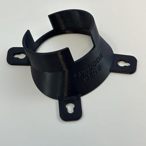 May include: A black, 3D-printed bracket with the text "OUTDOOR GEN2" on the side. The bracket has a circular opening and four mounting tabs with keyhole slots for easy installation. The design is made of a matte black plastic.