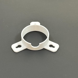 May include: A white plastic pipe clamp with a circular body and two wings with keyhole-shaped mounting holes. The clamp has a small tab on top and a notch at the bottom of the circle.