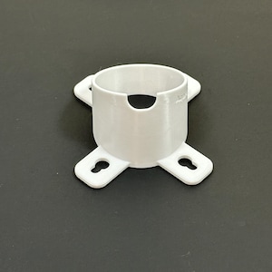 Puede incluir: Un objeto blanco impreso en 3D con un centro cilíndrico y cuatro brazos que sobresalen. Cada brazo tiene una abertura en forma de ojo de cerradura. El objeto está diseñado para sujetar o montar algo, posiblemente una lámpara u otro artículo similar.