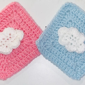 May include: Two crocheted squares, one pink and one blue, each with a white crocheted flower in the centre.