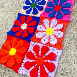 May include: A set of nine crocheted flower squares in various colors, including red, orange, yellow, blue, purple, and pink. Each square features a large, stylized flower with multiple petals.