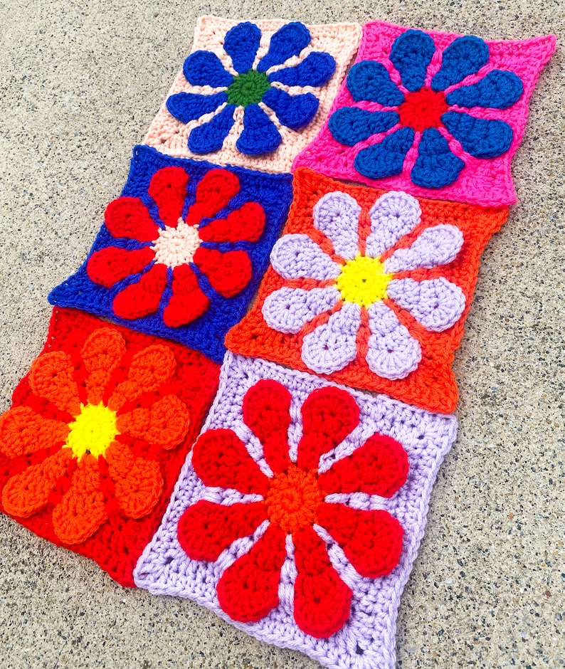 May include: A set of nine crocheted flower squares in various colors, including red, orange, yellow, blue, purple, and pink. Each square features a large, stylized flower with multiple petals.
