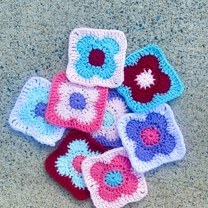 May include: A collection of crocheted squares featuring colourful flower designs in shades of pink, blue and red. The squares are made with a variety of stitches and textures.