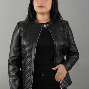 Könnte beinhalten: Eine schwarze Lederjacke mit einem gewebten Muster auf der Vorderseite und den Ärmeln. Die Jacke hat einen Reißverschluss und einen Stehkragen.