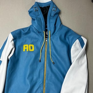May include: A blue leather jacket with white sleeves and yellow accents. The jacket has a hood and a zipper closure. The words "AO" are embroidered on the front of the jacket, and the word "GROWTH" is embroidered on the right sleeve.
