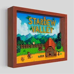 May include: A framed pixel art print of the video game Stardew Valley. The print features a farm scene with a farmhouse, a farmer riding a horse, a dog, and a chicken. The title "Stardew Valley" is written in large, pixelated letters at the top of the print.