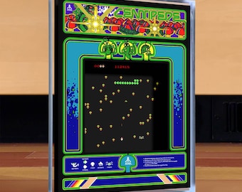 Puede incluir: Un mueble de juego de arcade Centipede enmarcado. El mueble presenta una pantalla negra que muestra los gráficos del juego, con un borde azul y verde. La parte superior del mueble tiene la palabra "Centipede" en verde, y el logotipo de Atari es visible.