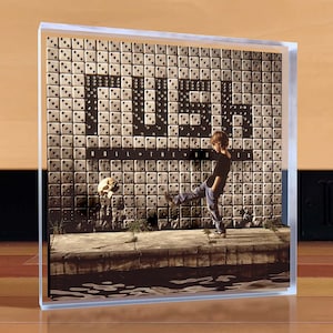 May include: Album cover featuring a boy kicking a soccer ball in front of a wall of dice. The word "FUZZ" is displayed in large letters, with "ROLL THE BONES" below. The image is encased in a clear acrylic block.