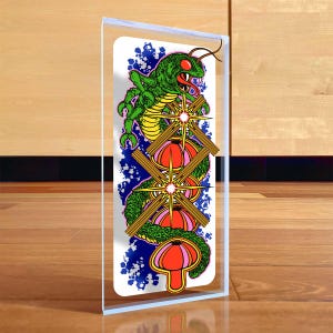 Peut inclure: Bloc de verre rectangulaire avec une illustration colorée d'un serpent vert aux yeux rouges et aux écailles jaunes. Le serpent est enroulé autour de deux objets rouges et jaunes avec des éclats d'étoiles. Le fond présente des éclaboussures bleues.