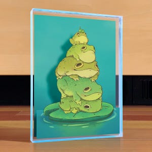 Peut inclure: Une impression d'art encadrée représentant une pile de grenouilles de dessin animé. Les grenouilles sont de différentes nuances de vert et sont empilées les unes sur les autres, la grenouille du bas reposant sur une feuille de nénuphar. Le fond est turquoise.