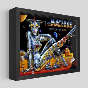 May include: Framed artwork featuring a retro pinball machine theme. The image showcases a metallic robot woman with the text "THE MACHINE BRIDE OF PIN BOT." The artwork is set against a space-themed background with planets and a red surface.