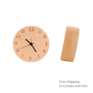May include: A round light-colored wooden clock featuring engraved numerals from 1 to 12 and black clock hands. The clock is shown from a front-facing perspective and a side-view perspective, highlighting the smooth, natural wood grain texture of the casing.