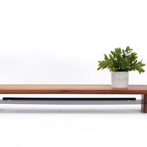 May include: A wooden shelf with a metal bar underneath. The shelf is brown and the bar is gray. A small potted plant is on the shelf.
