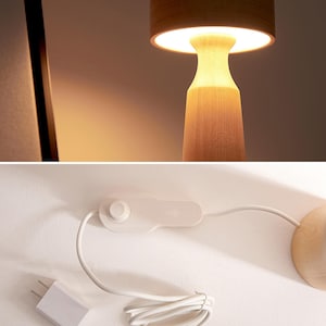 K&ouml;nnte beinhalten: Eine Tischlampe aus Holz mit einem pilzf&ouml;rmigen Schirm. Die Lampe hat ein wei&szlig;es Kabel mit einem Schalter und einem USB-Stecker. Die Lampe steht auf einer wei&szlig;en Oberfl&auml;che.