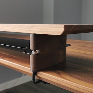 May include: A wooden desk with a black metal shelf attached to the underside. The shelf is designed to hold items like a keyboard or mouse.