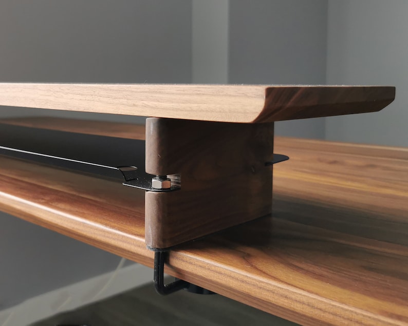 May include: A wooden desk with a black metal shelf attached to the underside. The shelf is designed to hold items like a keyboard or mouse.